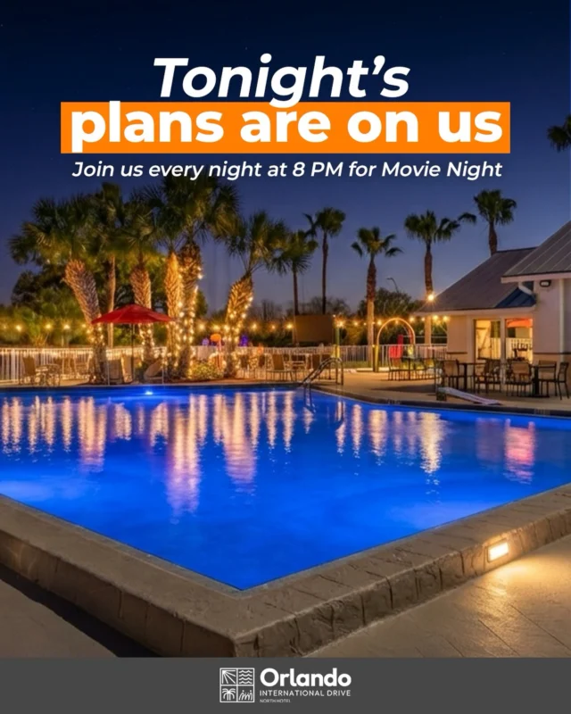 A nighttime view of a hotel pool with blue water, surrounded by palm trees and outdoor furniture, with string lights and a dark sky.