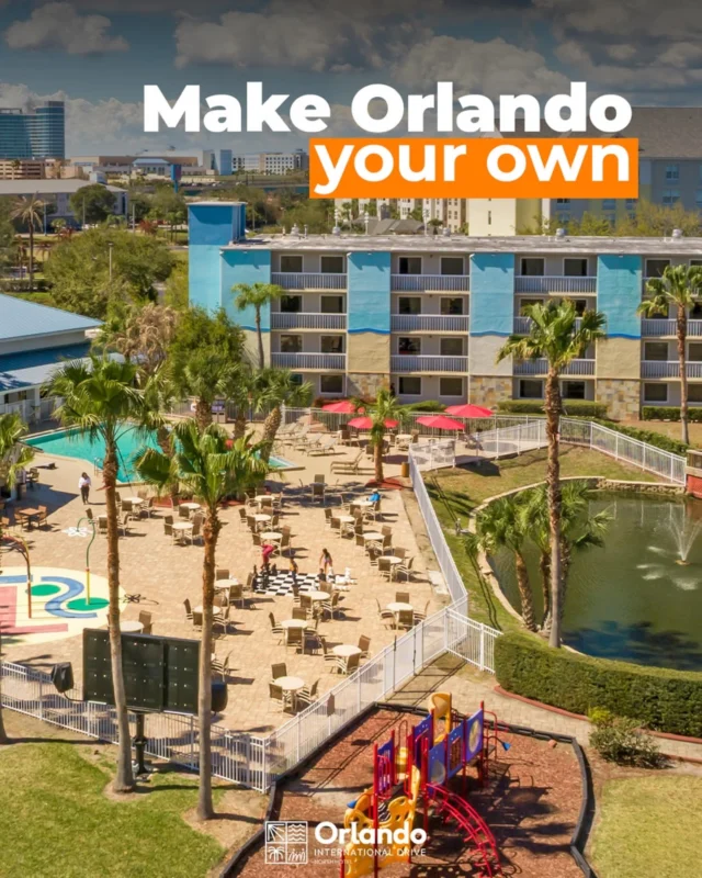 Aerial view of a hotel with a pool area, playground, and palm trees